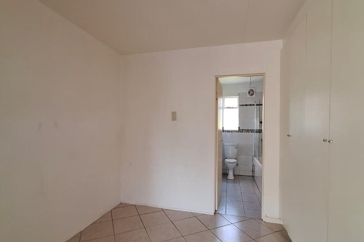 A bedroom featuring built-in cupboards and tiled flooring, with an adjoining en-suite bathroom visible through the doorway.