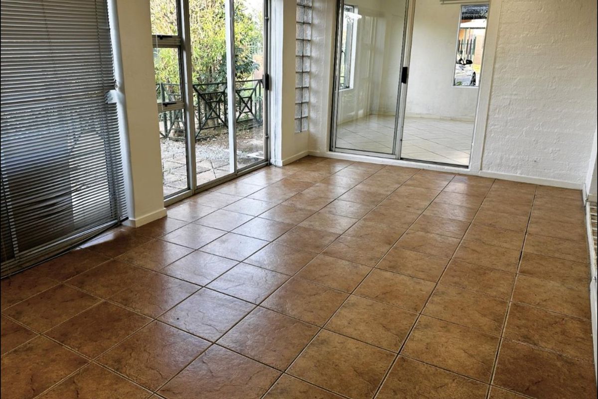 A bright, empty living area featuring ceramic floor tiles, large sliding glass doors providing outdoor access, and a decorative glass block wall section.