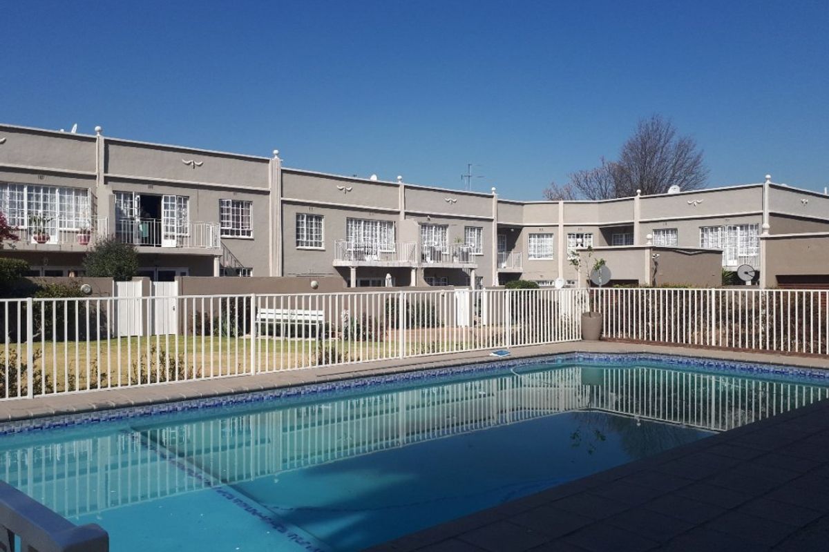 A communal swimming pool area set within a well-maintained apartment complex, featuring paved surrounds and secure perimeter fencing.