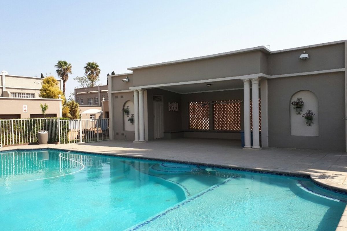 A spacious covered patio area overlooking a private swimming pool, featuring classic architectural columns and tiled flooring.
