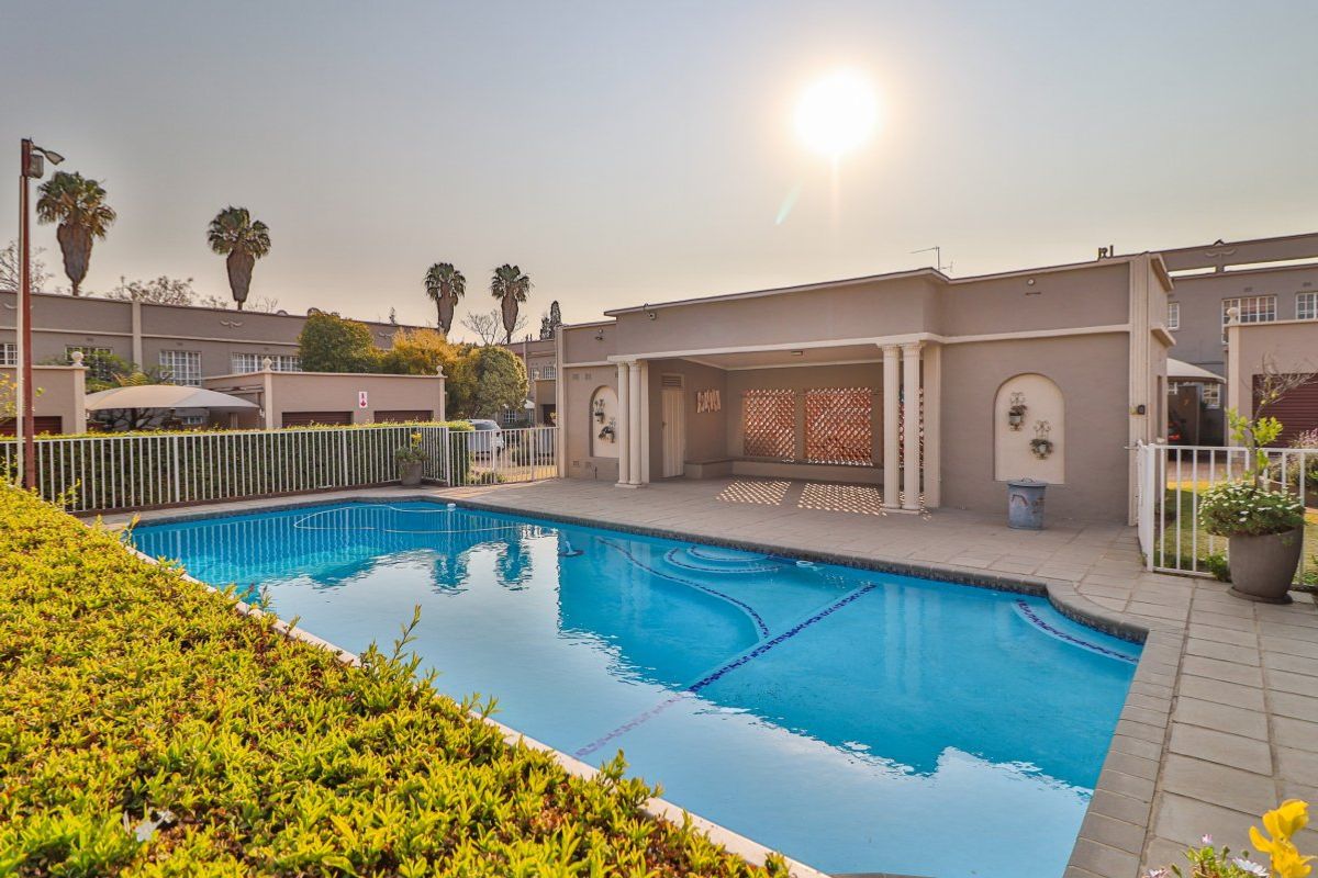 A well-maintained communal swimming pool area featuring paved decking, decorative columns, and a covered outdoor entertainment space within the apartment complex.