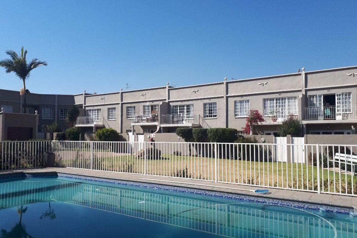 A view of the apartment complex exterior featuring a communal swimming pool, fenced garden area, and private balconies for the upper-level units.