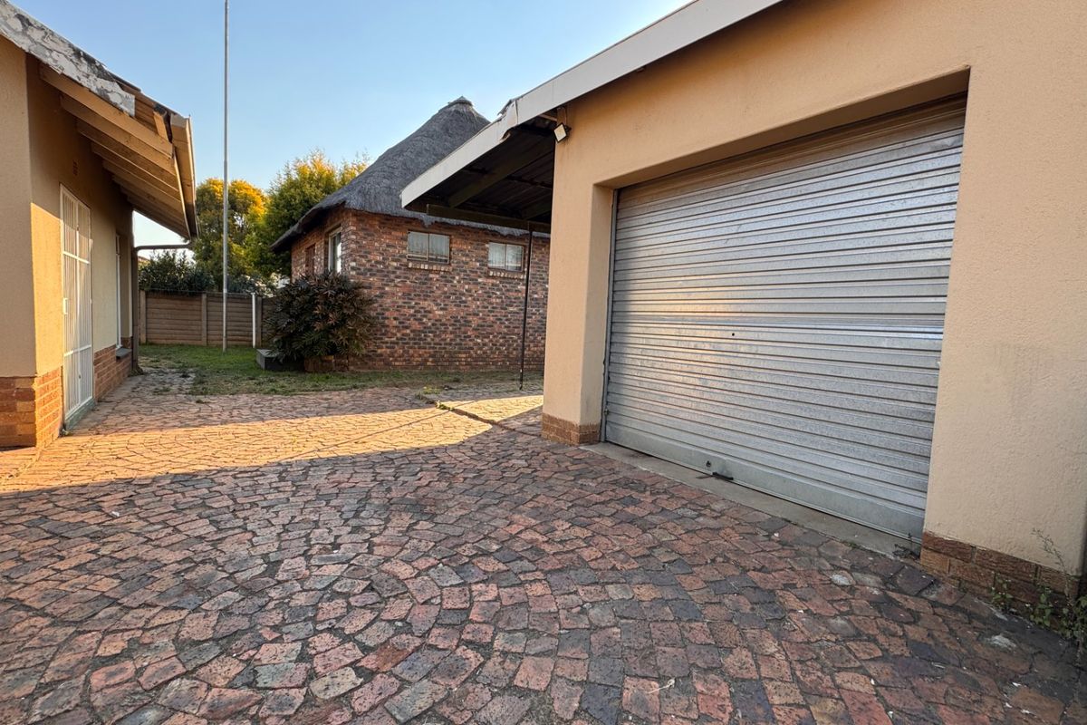 Exterior view of the property featuring a paved driveway, a roller shutter garage door, and a separate brick structure with a thatched roof.