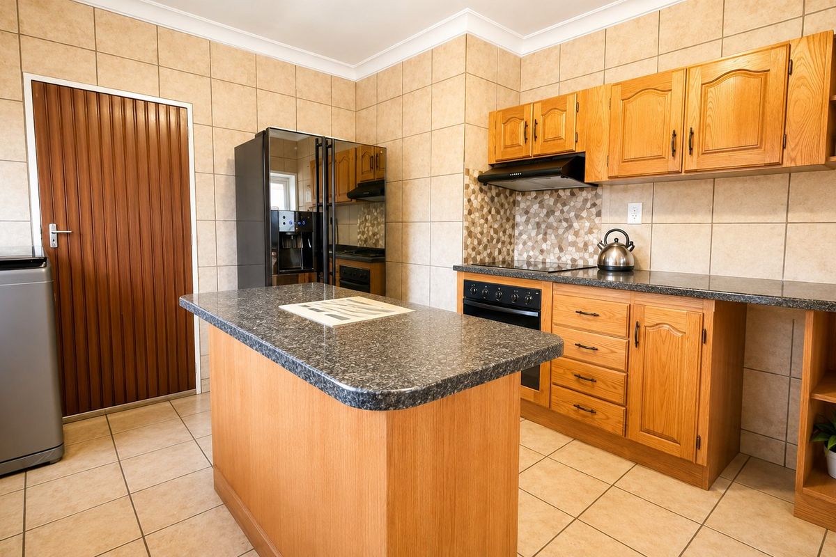 A functional kitchen featuring wooden cabinetry, a central island with a stone-look countertop, tiled walls, and built-in oven and extractor fan.