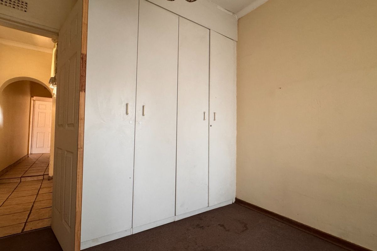 A bedroom featuring built-in cupboards and carpeted flooring, with a view into the adjacent hallway.