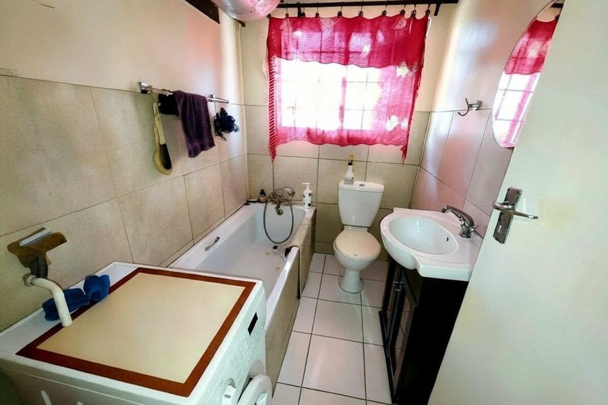 Compact bathroom featuring a bathtub, pedestal vanity, and toilet, with tiled walls and flooring, providing essential utility in a functional layout.