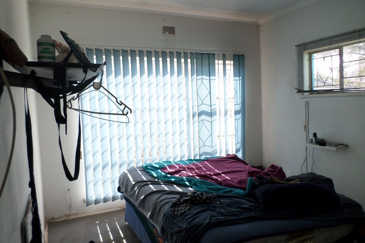 A bedroom featuring a large window with vertical blinds, a smaller side window, and basic wall finishes.