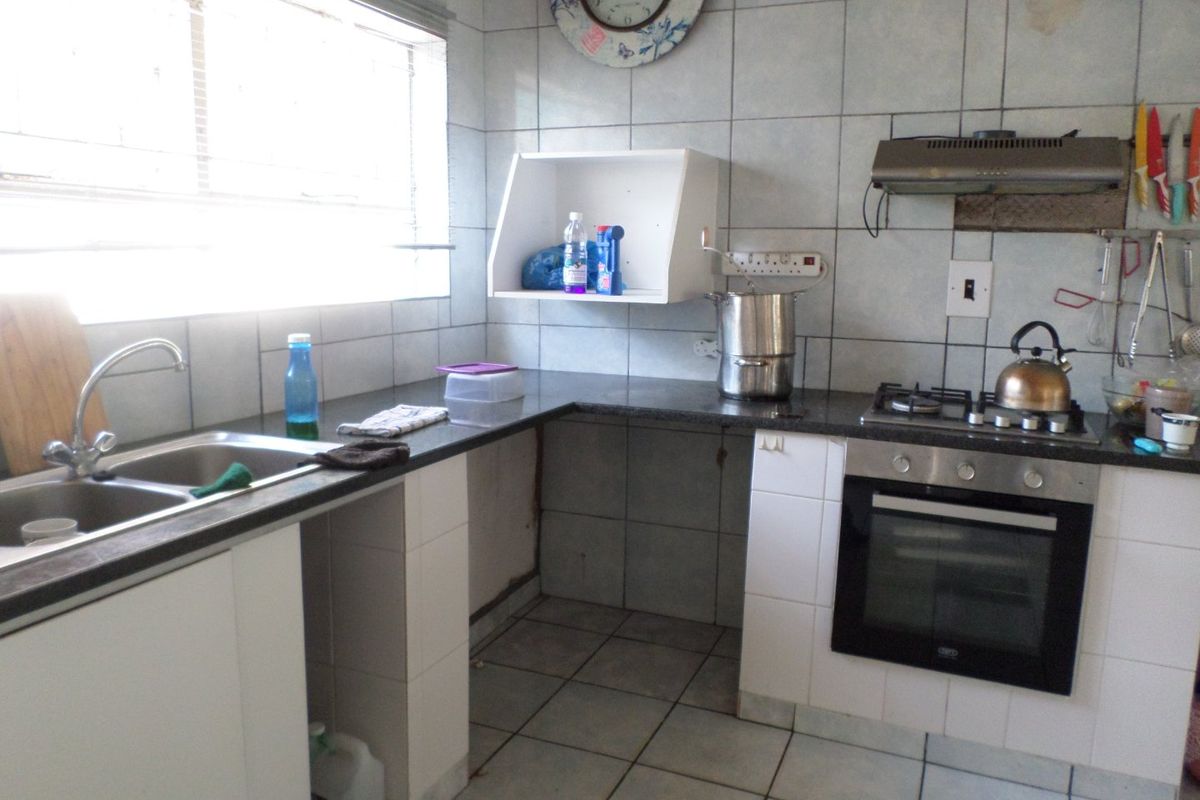 A functional kitchen featuring tiled walls, granite countertops, a built-in oven, gas hob, extractor fan, and a double-basin sink.