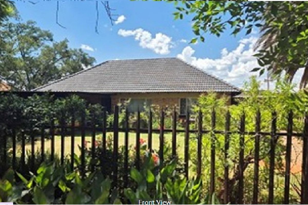 A front view of a single-story residential house featuring a tiled roof, brick facade, and a secure metal perimeter fence.