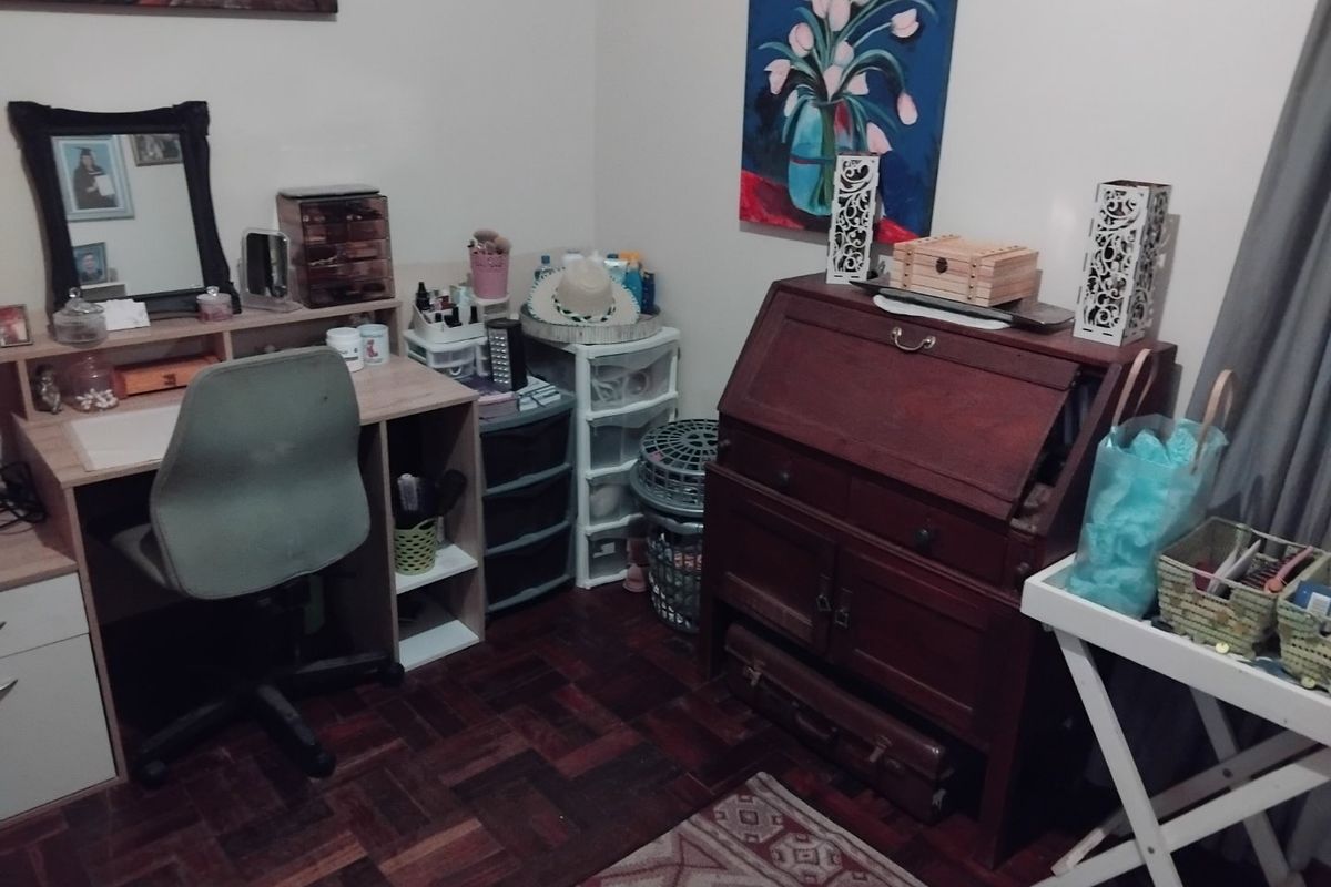 A functional bedroom space featuring dark parquet wood flooring and neutral wall finishes, currently utilized as a home office or dressing area.