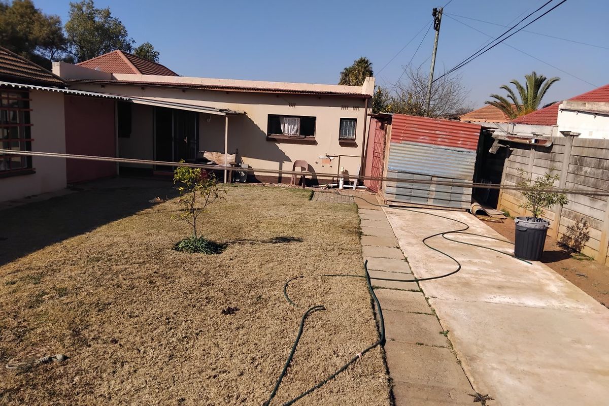 Rear view of the property featuring a paved walkway, a small lawn area, and a corrugated metal storage structure attached to the main building.