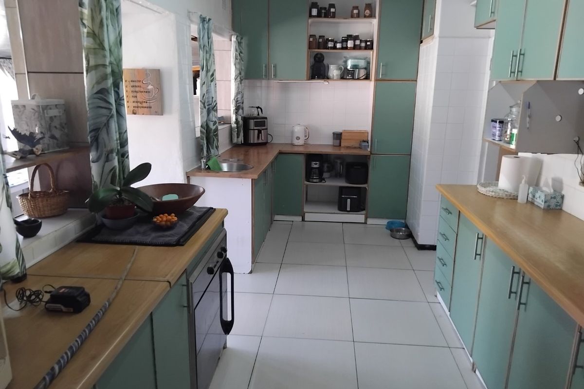 A functional kitchen featuring light green cabinetry, wood-look countertops, tiled flooring, and built-in oven and hob.