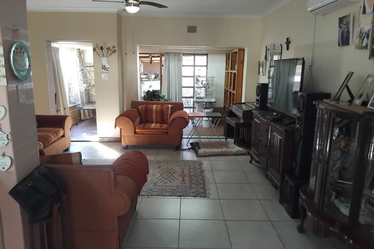 Spacious living area featuring tiled flooring, a ceiling fan, and a wall-mounted air conditioning unit, with direct access to an adjoining sunroom.