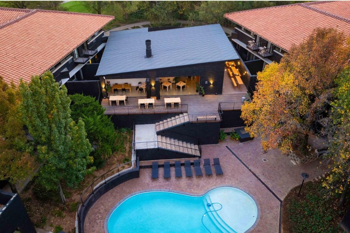 Aerial view of a modern apartment complex featuring a central clubhouse, swimming pool, paved courtyard, and landscaped surroundings.