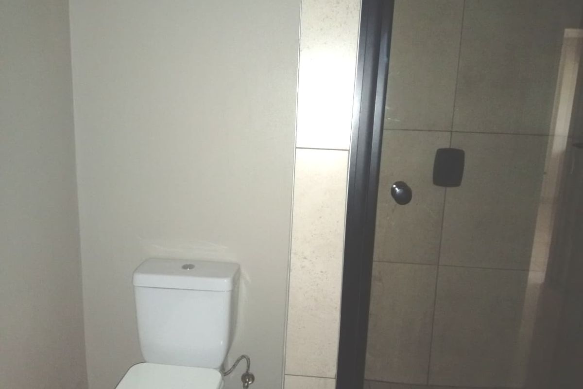 A functional bathroom featuring a modern toilet and a tiled shower enclosure with dark frame detailing.