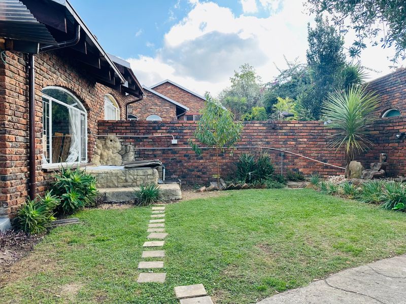 A private rear garden featuring a face brick facade, a stone-look built-in feature, and a paved pathway leading across the lawn.