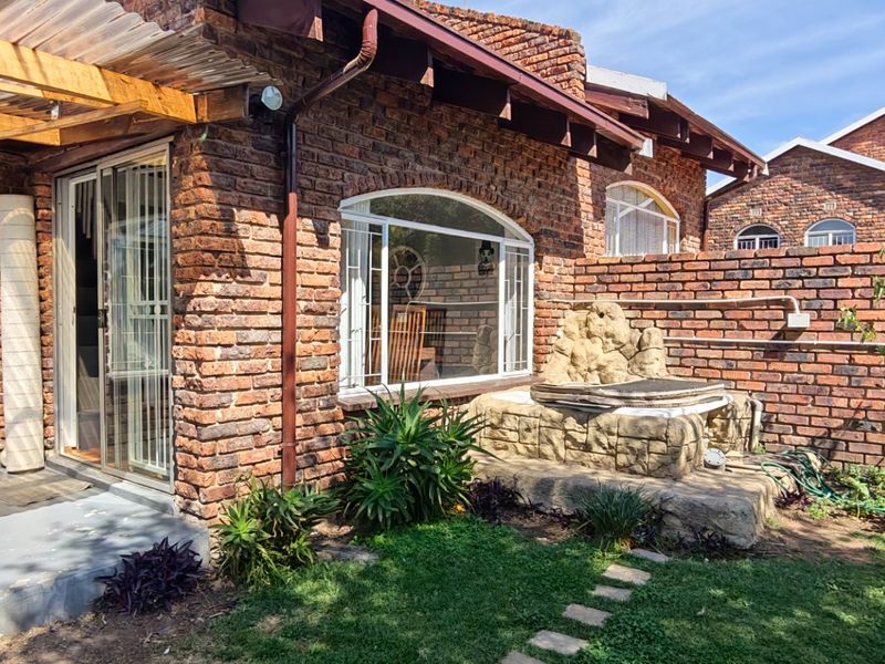 Rear exterior view of a face brick townhouse featuring a covered patio, sliding glass doors, and a private garden with a stone water feature.