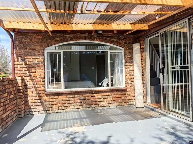 A covered outdoor patio featuring exposed brick walls, a timber pergola with a corrugated roof, and direct access to the interior via sliding glass doors.