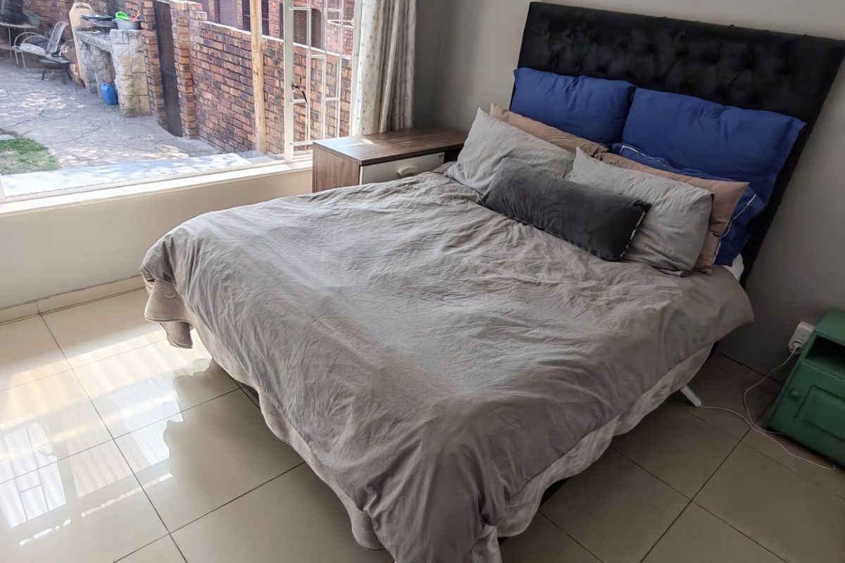 A bedroom featuring tiled flooring and a large window providing natural light and views of the rear exterior area.