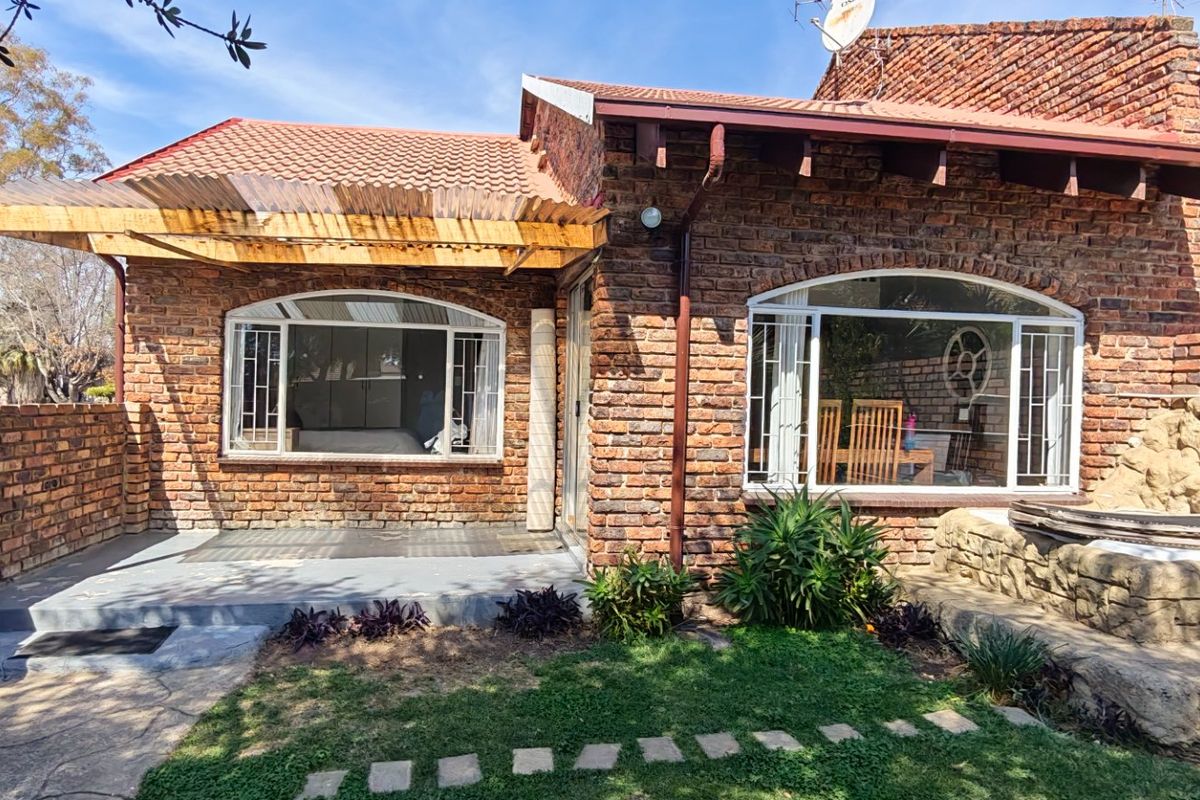 Rear view of a face brick townhouse featuring a covered patio, arched windows, and a stone water feature set within a small garden area.