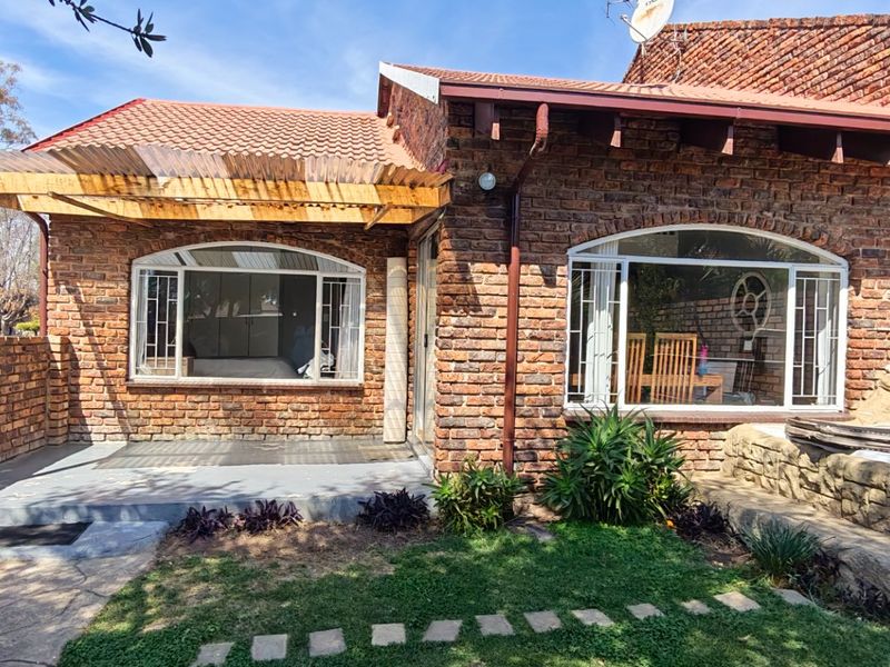 Rear view of a face brick townhouse featuring a covered patio, arched windows, and a stone water feature set within a small garden area.