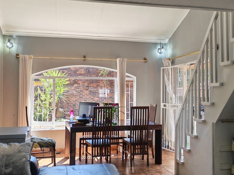Open plan living and dining area featuring a staircase, vaulted ceilings, tiled flooring, and an arched window overlooking the rear garden.