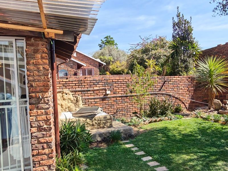 A private rear garden featuring a brick boundary wall, a small lawn, and a covered patio area with a sliding glass door entrance.
