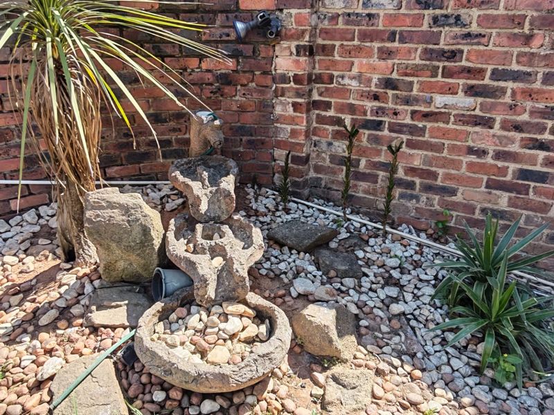 A small garden corner featuring a stone water feature set against a rustic brick boundary wall with pebble landscaping.