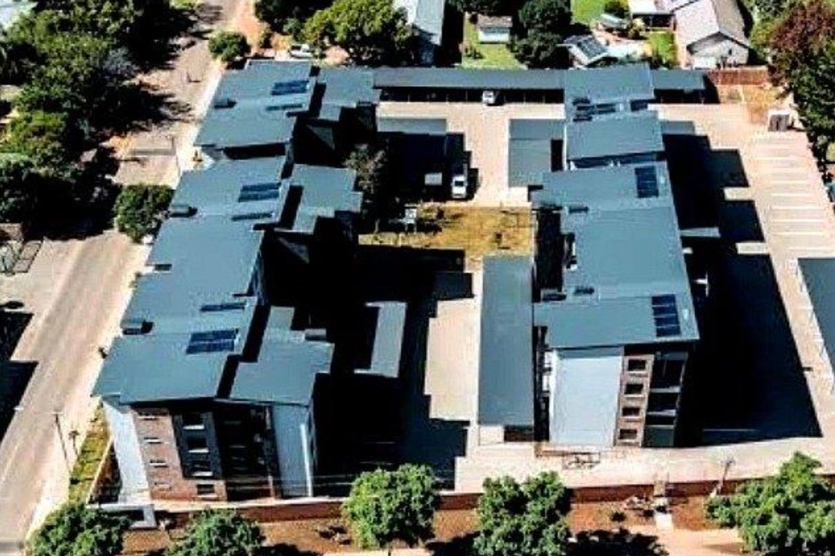 Aerial view of the apartment complex featuring multiple buildings with metal roofing, solar panels, and dedicated paved parking areas.