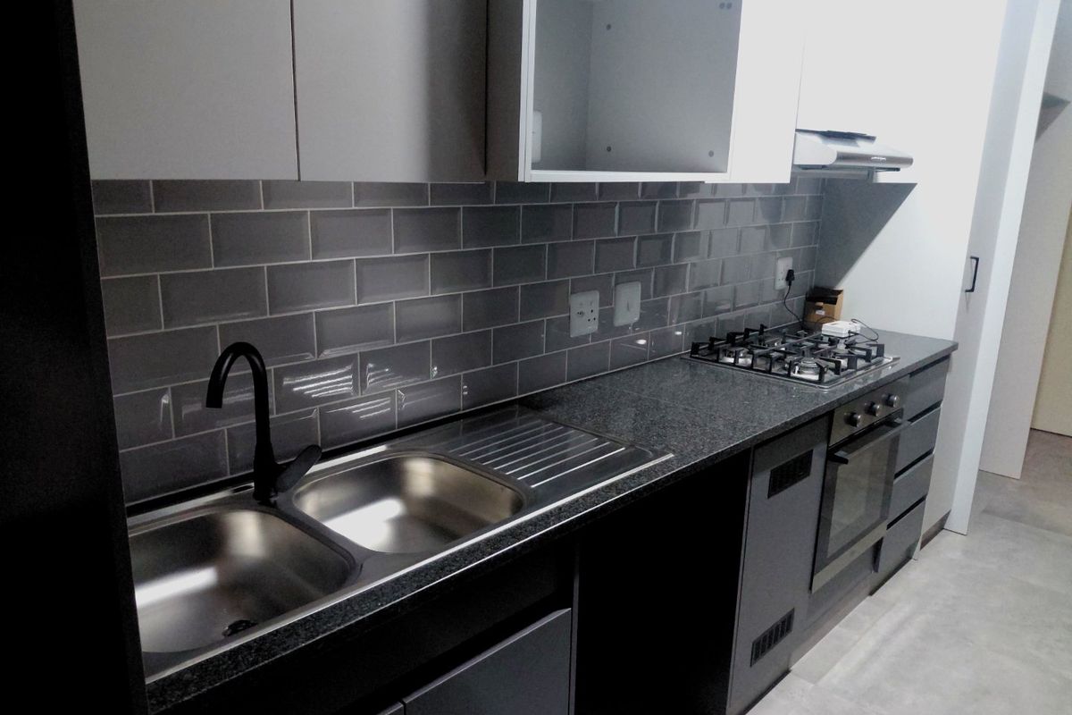 Modern kitchen featuring sleek grey cabinetry, subway tile backsplash, granite countertops, stainless steel double sink, and integrated gas hob with oven.