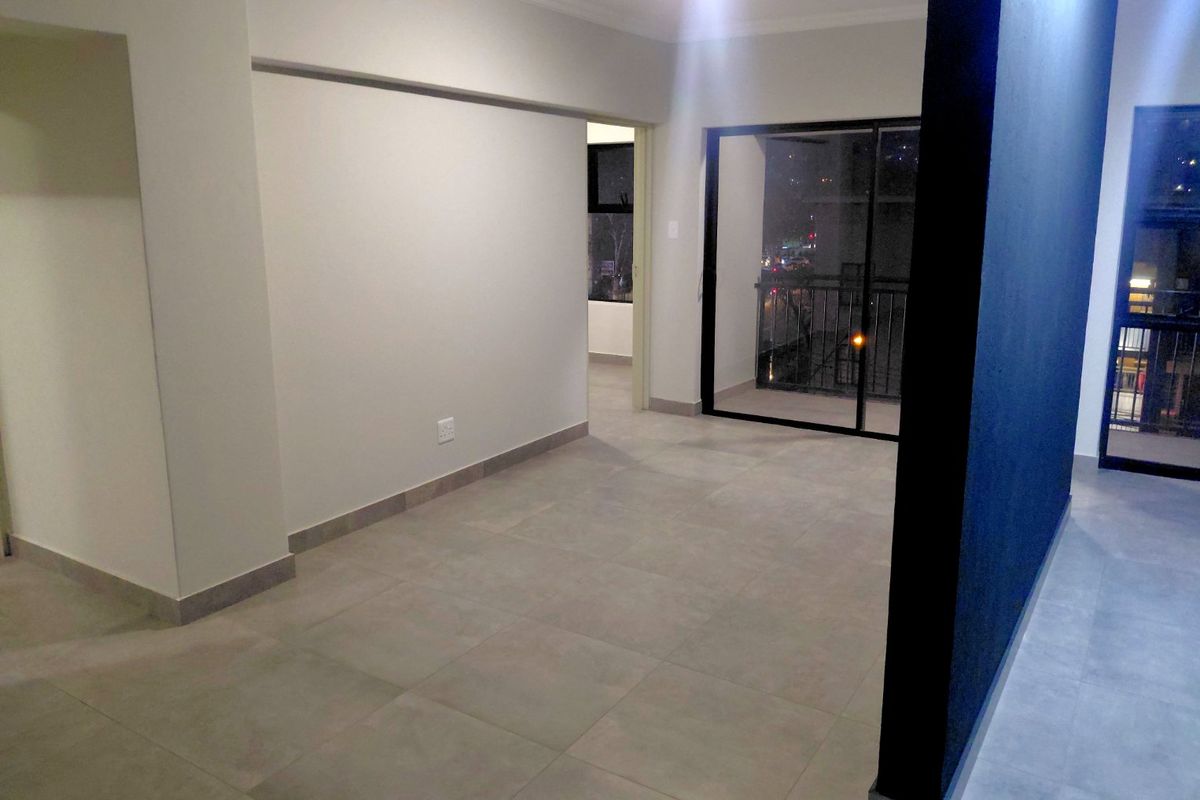 An empty, modern living area featuring neutral tiled flooring, clean white walls, and a sliding glass door providing access to a balcony.