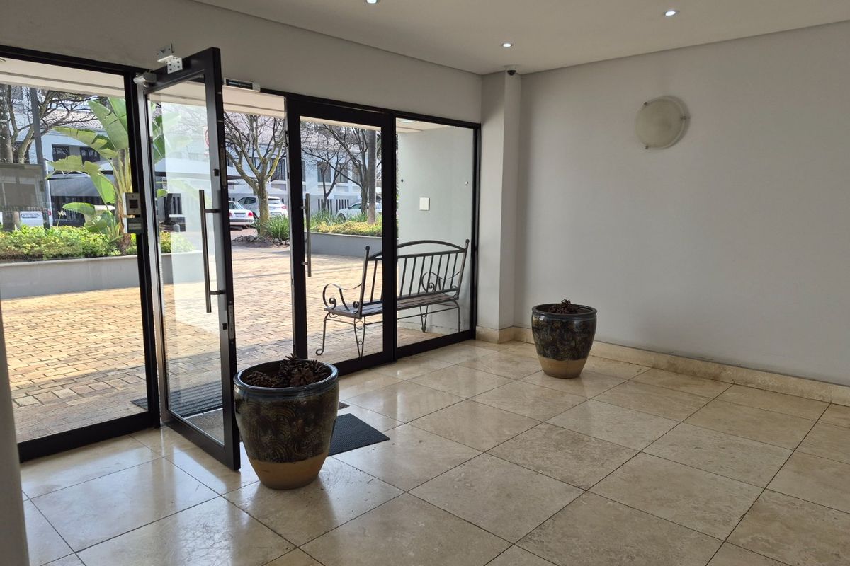 A bright and spacious commercial entrance lobby featuring polished tile flooring, recessed lighting, and large glass doors providing access to the exterior.