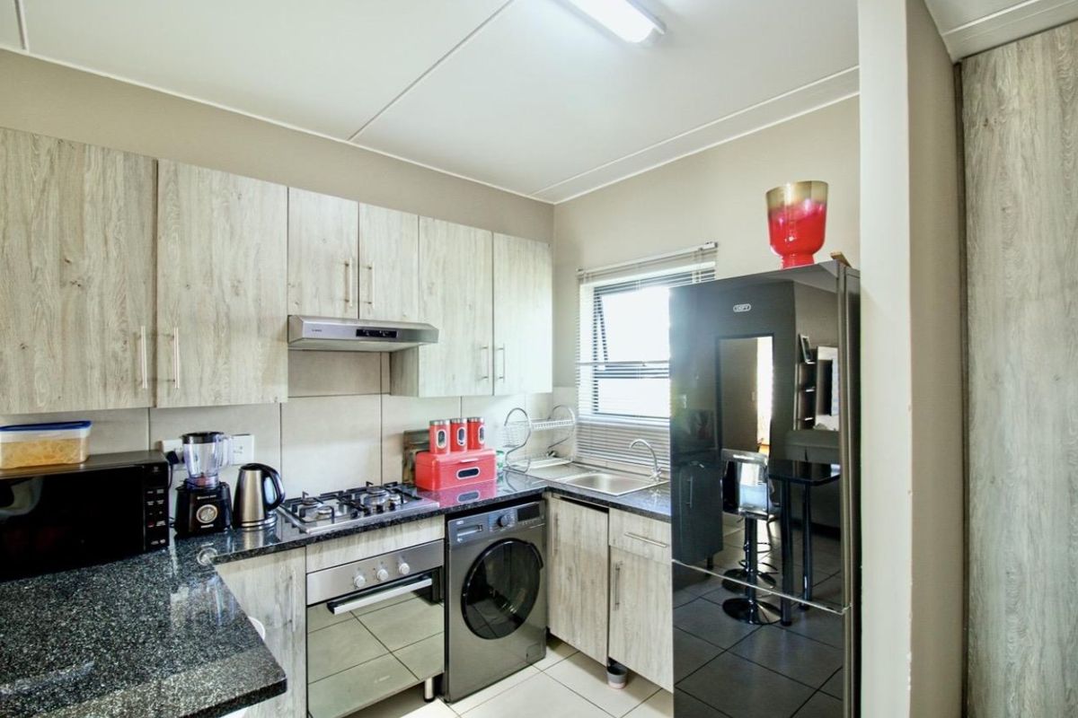 A functional kitchen featuring light wood-grain cabinetry, granite countertops, a gas hob, built-in oven, and integrated space for a washing machine.