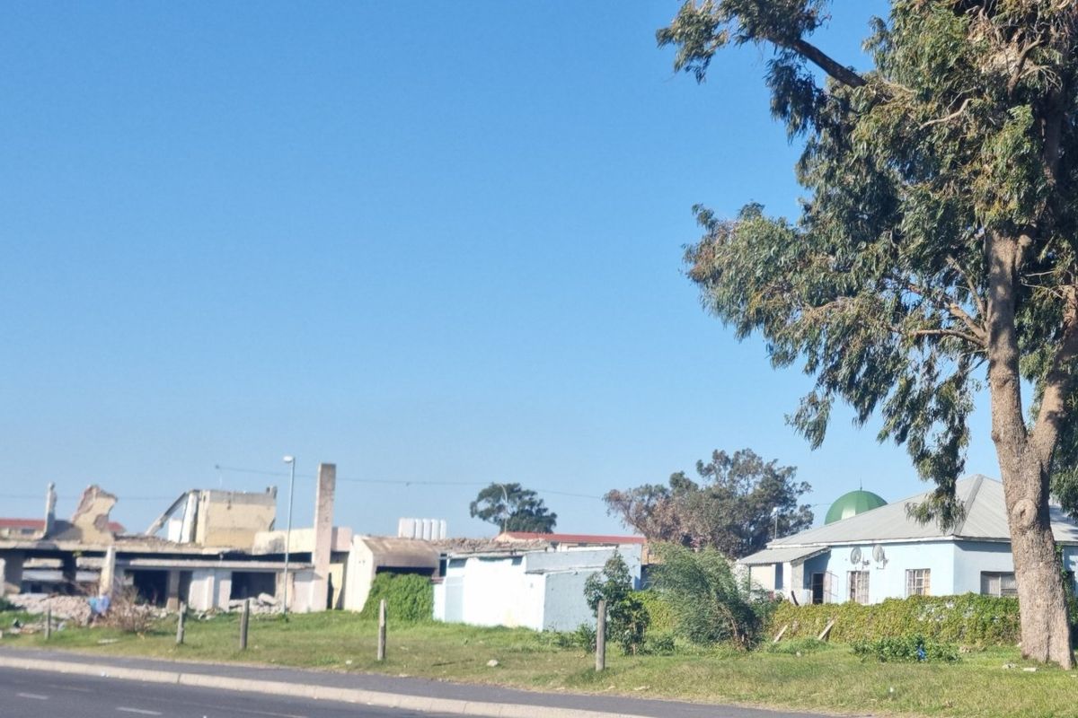 Street view of a residential plot featuring a mature tree and the remains of a demolished building structure.