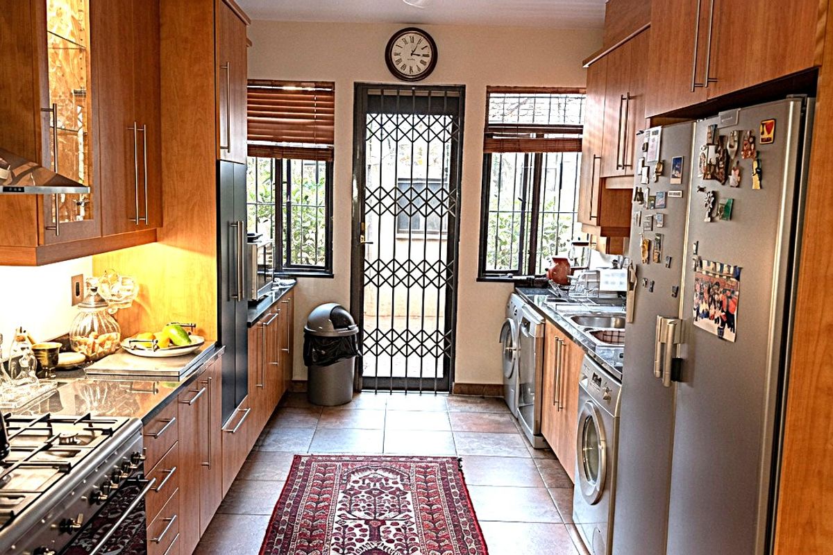 A functional galley-style kitchen featuring wooden cabinetry, a gas stove with extractor, tiled flooring, and direct access to an outdoor area via a security gate.