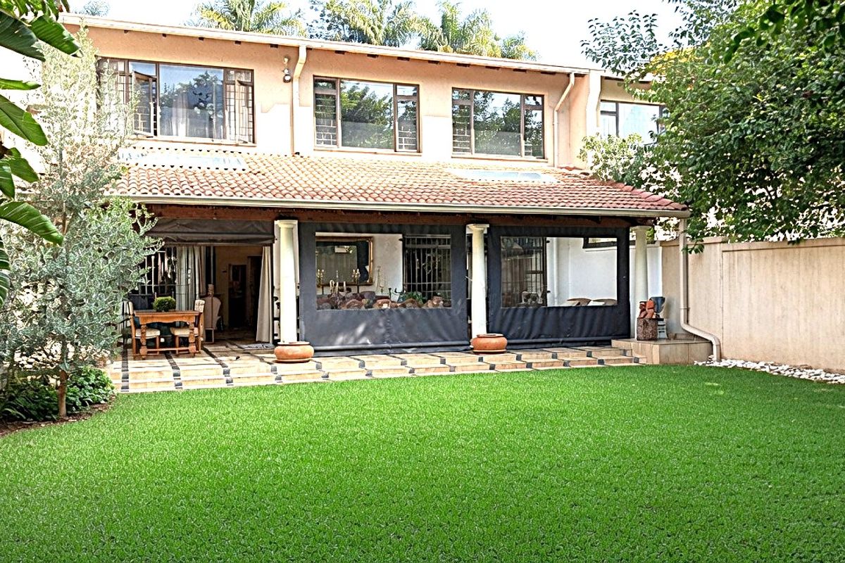 Rear view of the townhouse featuring a covered patio with tiled flooring, support columns, and a well-maintained private garden lawn.
