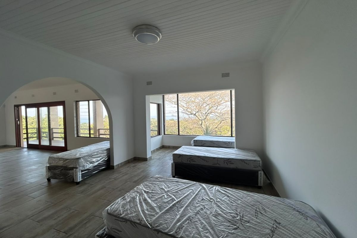 Spacious bedroom featuring large picture windows, timber-look tiled flooring, and an arched entryway leading to an adjoining space.
