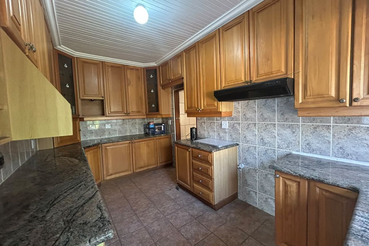A functional kitchen featuring extensive wooden cabinetry, granite countertops, tiled backsplash, and a tongue and groove ceiling, offering a classic layout ready for modernization.