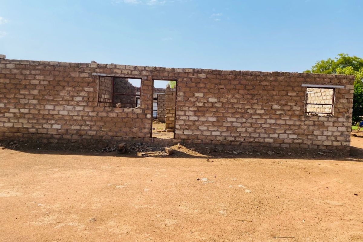 An unfinished brick structure showing exposed masonry walls with open window and door frames, currently in a shell state of construction.
