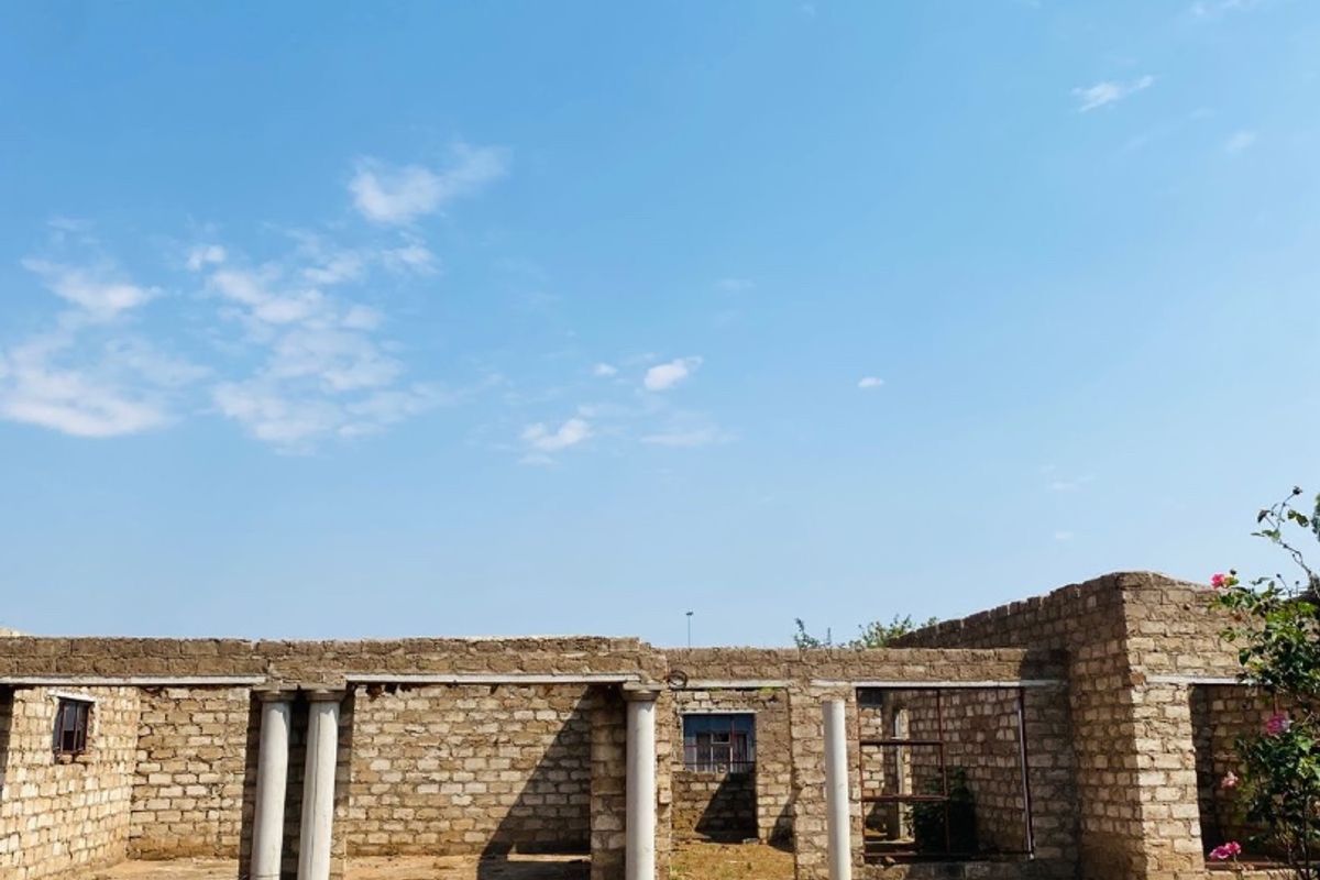 An unfinished residential structure featuring exposed brick walls and concrete columns, currently in a shell state awaiting completion and roofing.