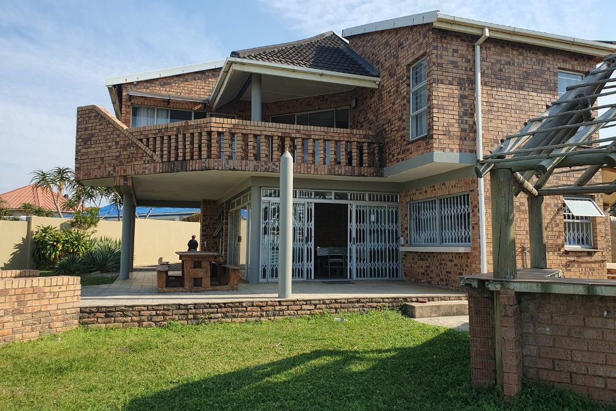 Rear view of a double-story face brick house featuring a covered patio, upper-level balcony, and a timber pergola structure in the garden.