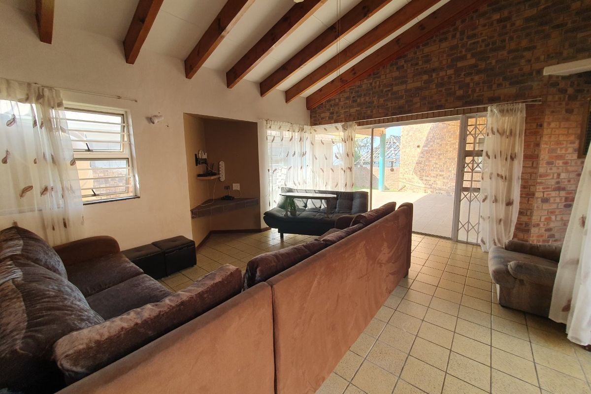Spacious living room featuring exposed timber ceiling beams, a brick feature wall, tiled flooring, and direct access to the outdoor patio area.