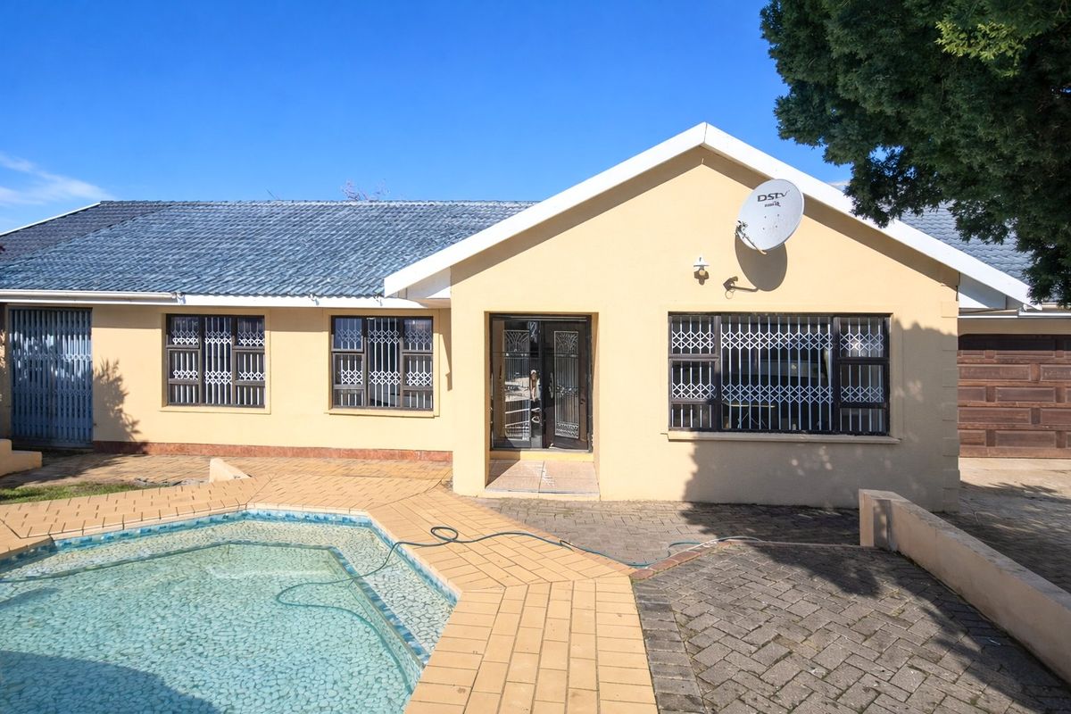 Rear view of the house featuring a swimming pool, paved patio area, and secure window bars.
