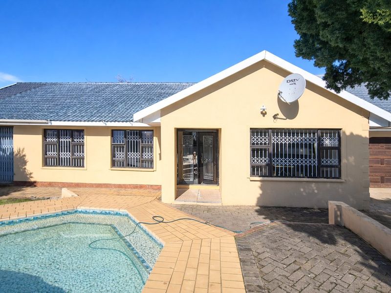 Rear view of the house featuring a swimming pool, paved patio area, and secure window bars.