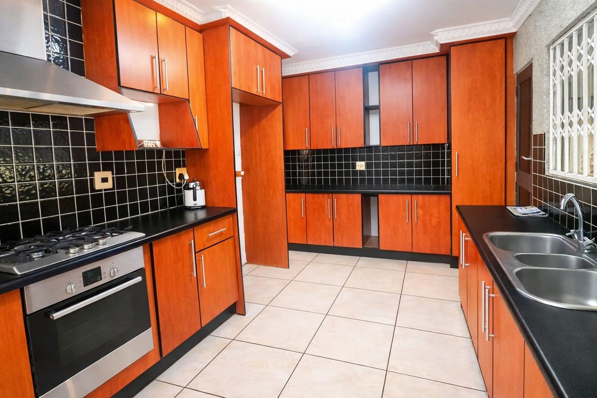A functional kitchen featuring wooden cabinetry, black tiled splashbacks, a gas hob with extractor, and a double bowl sink with ample counter space.
