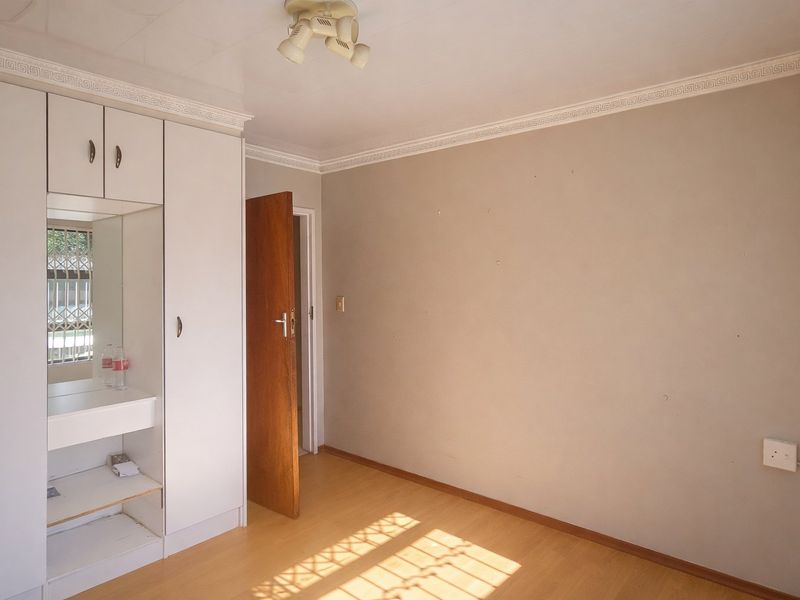 A vacant bedroom featuring laminate flooring, built-in cupboards with a vanity mirror, and decorative ceiling cornicing.