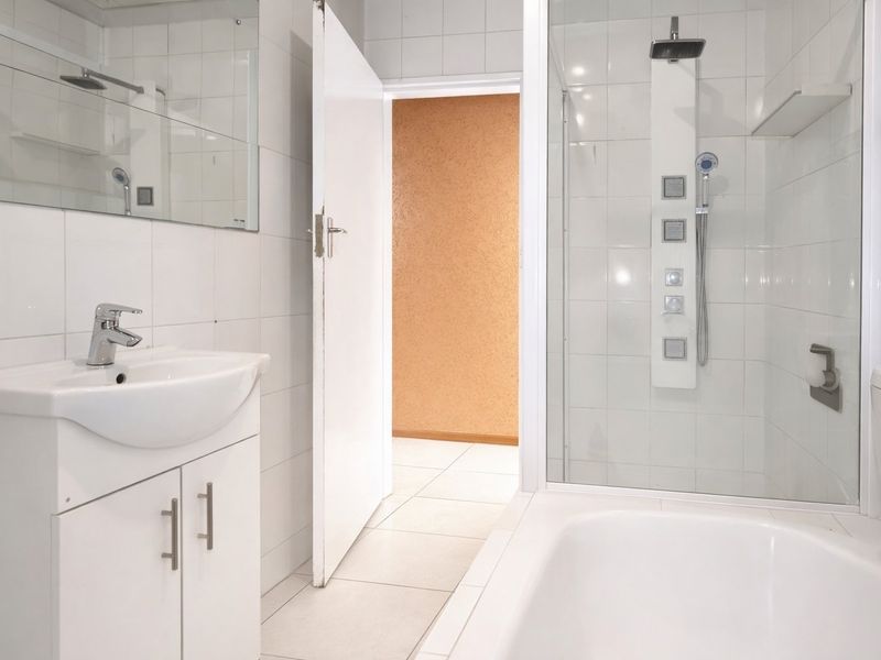 A clean, modern bathroom featuring a white vanity, a glass-enclosed shower with a panel system, a bathtub, and neutral ceramic tiling throughout.