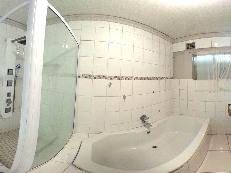 A spacious bathroom featuring a shower enclosure, built-in bathtub, toilet, and vanity basin, requiring some cosmetic repairs to wall finishes and tiling.