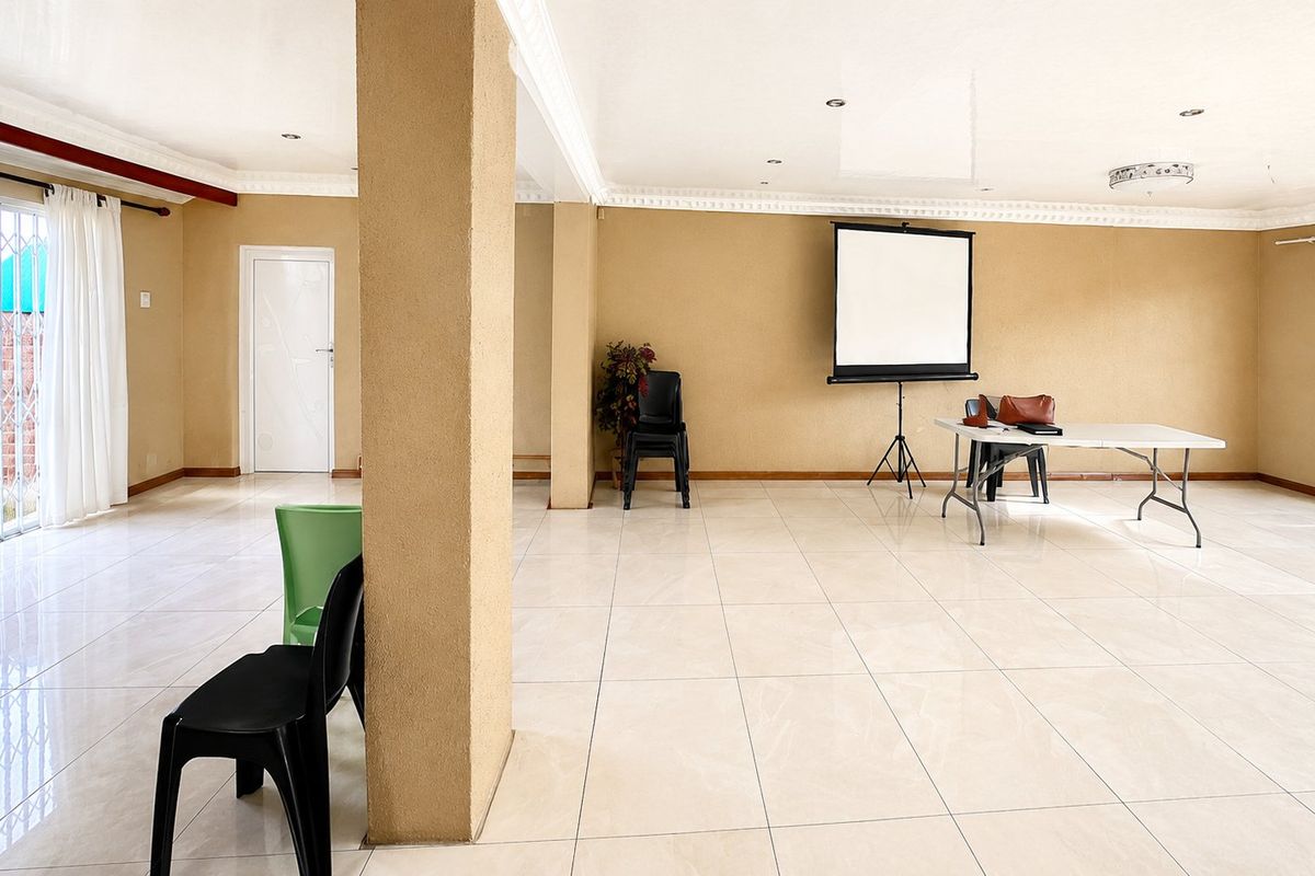 Spacious open-plan living area featuring neutral wall tones, large format floor tiles, decorative ceiling cornices, and access to the exterior via a sliding door.