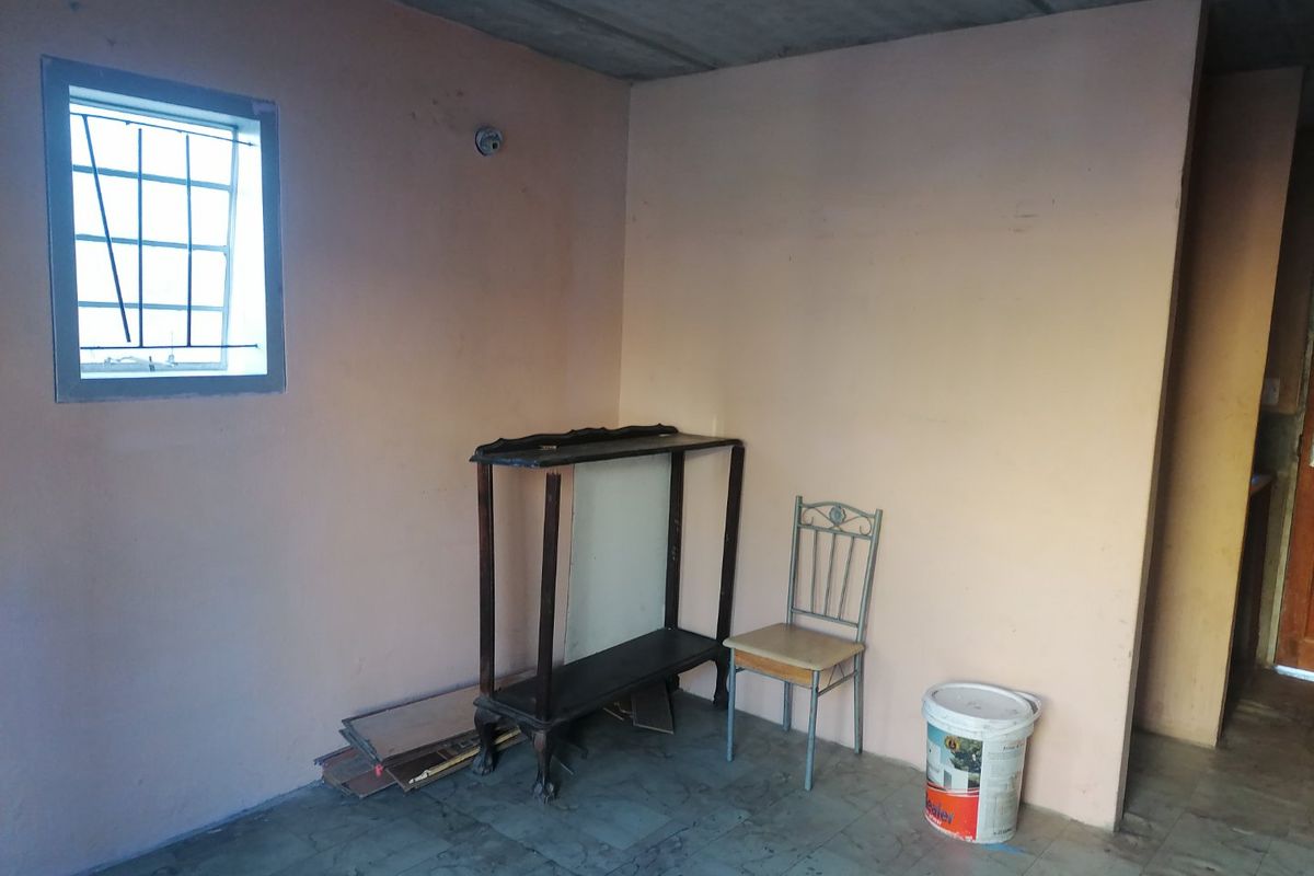 A basic living area featuring tiled flooring, security bars on the window, and an unfinished exposed concrete ceiling.
